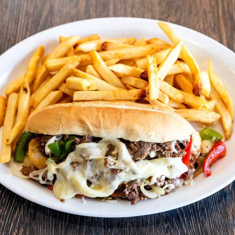 A philly cheesesteak sandwich served with fries